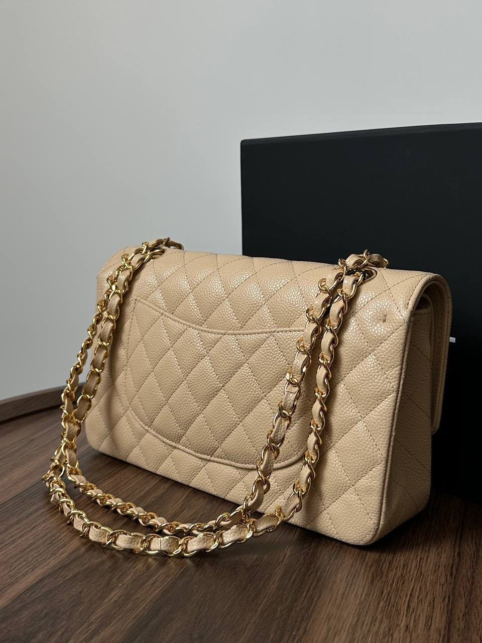Beige quilted handbag with gold chain on a wooden surface