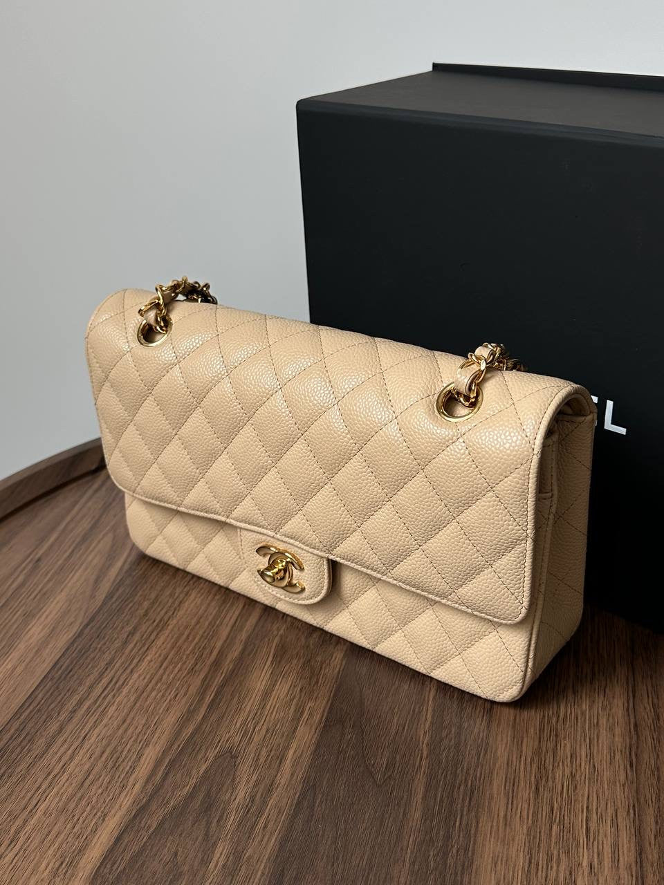 Beige quilted handbag with gold hardware on a wooden surface with a black box in the background.