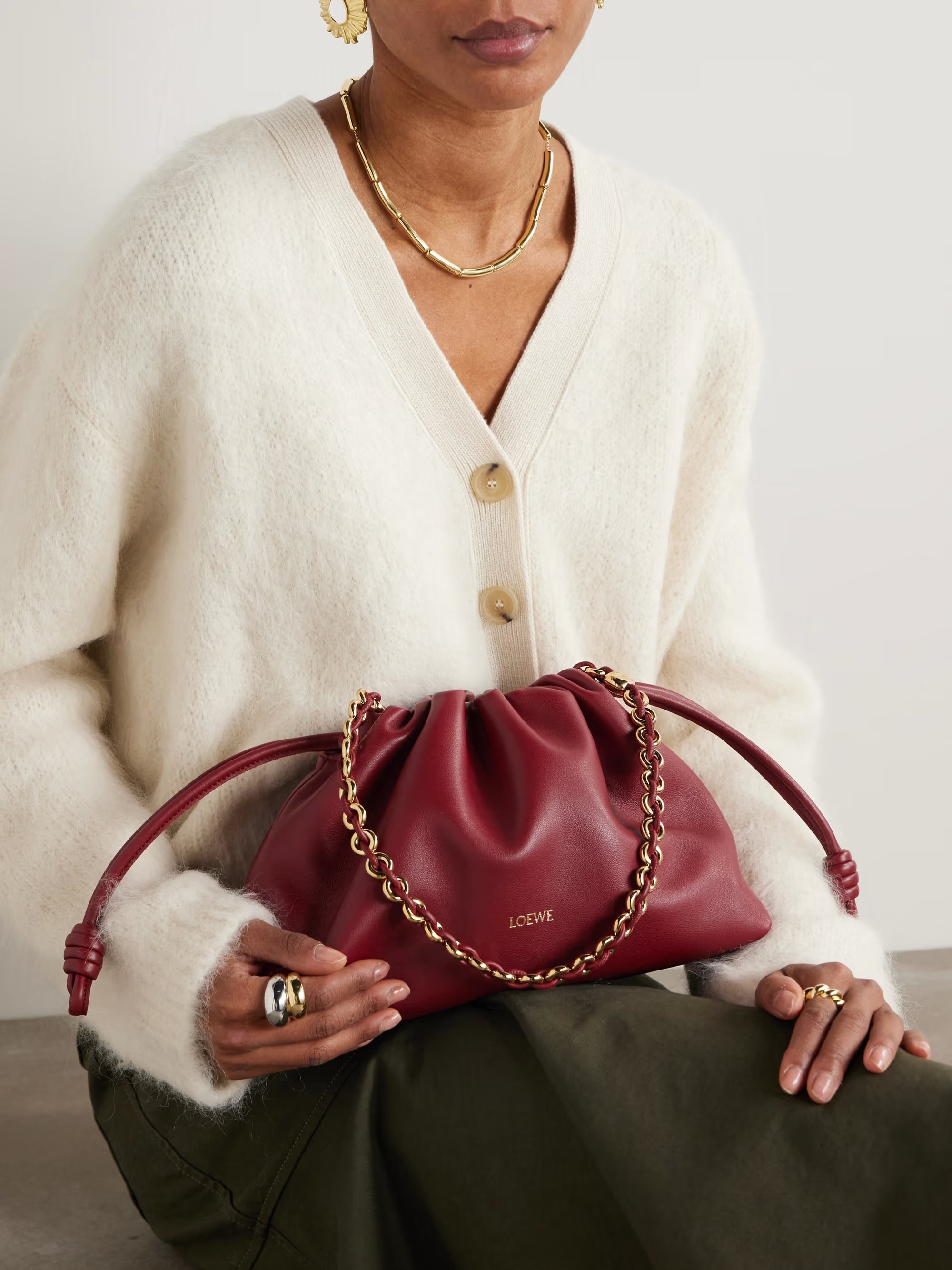 Person holding a red handbag with gold chain detail, wearing a white sweater and gold jewelry.