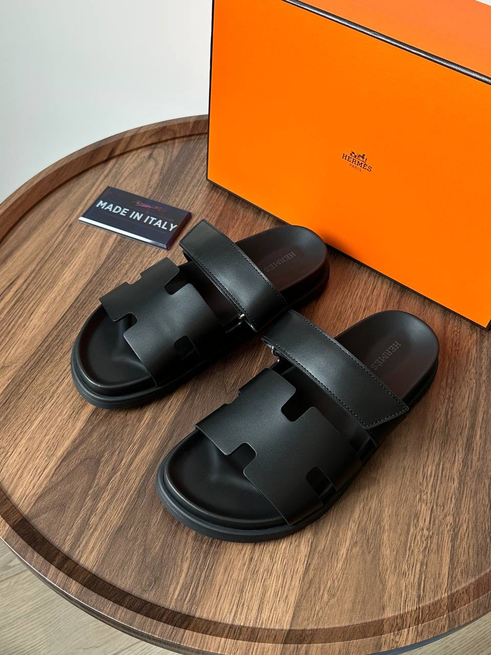Black sandals on a wooden surface with an orange box in the background